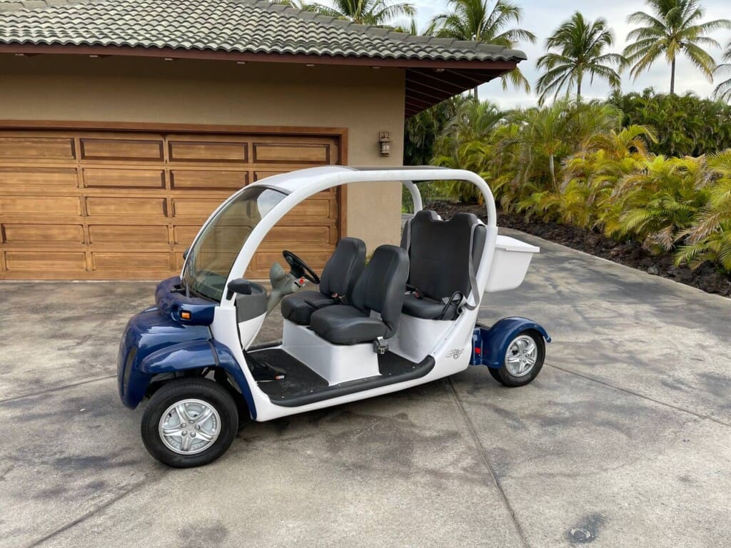 A white and blue GEM electric golf cart parked on a concrete driveway in front of a wooden garage door.