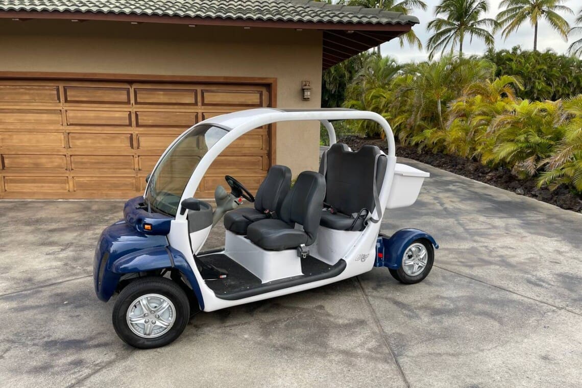 A white and blue GEM electric golf cart parked on a concrete driveway in front of a wooden garage door.