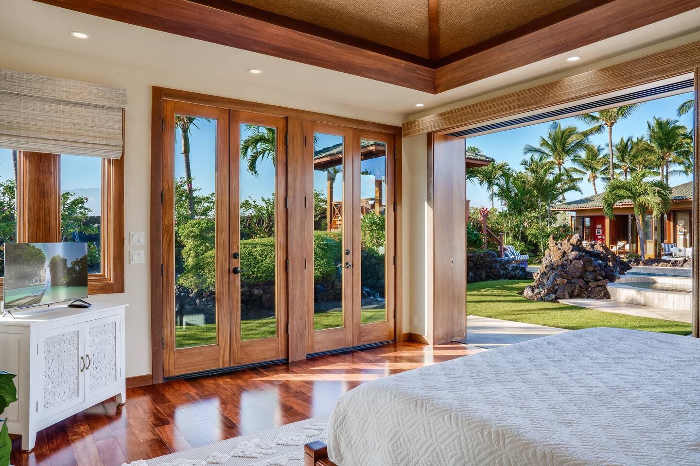 View from the primary bedroom at Hale Mele overlooking the private lanai, tropical gardens, and pool in Mauna Lani.