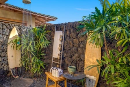 Private outdoor shower surrounded by lava rock walls and tropical plants beside Bedroom 2 at Hale Mele, a luxury vacation rental in Mauna Lani on the Big Island of Hawaiʻi.
