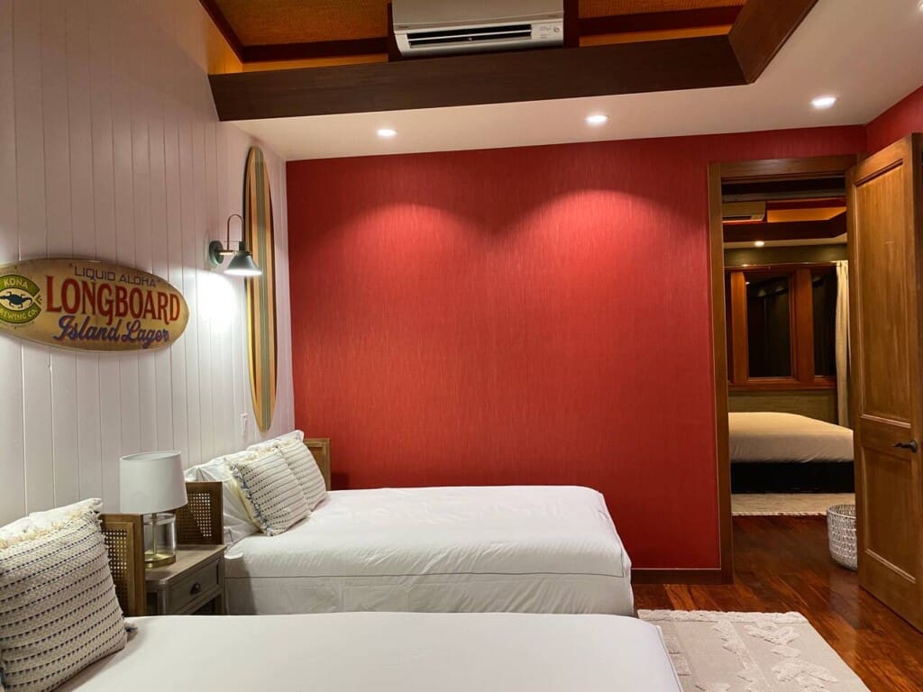 A bedroom with two beds, a red accent wall, and an open doorway providing a view into an adjacent bedroom.