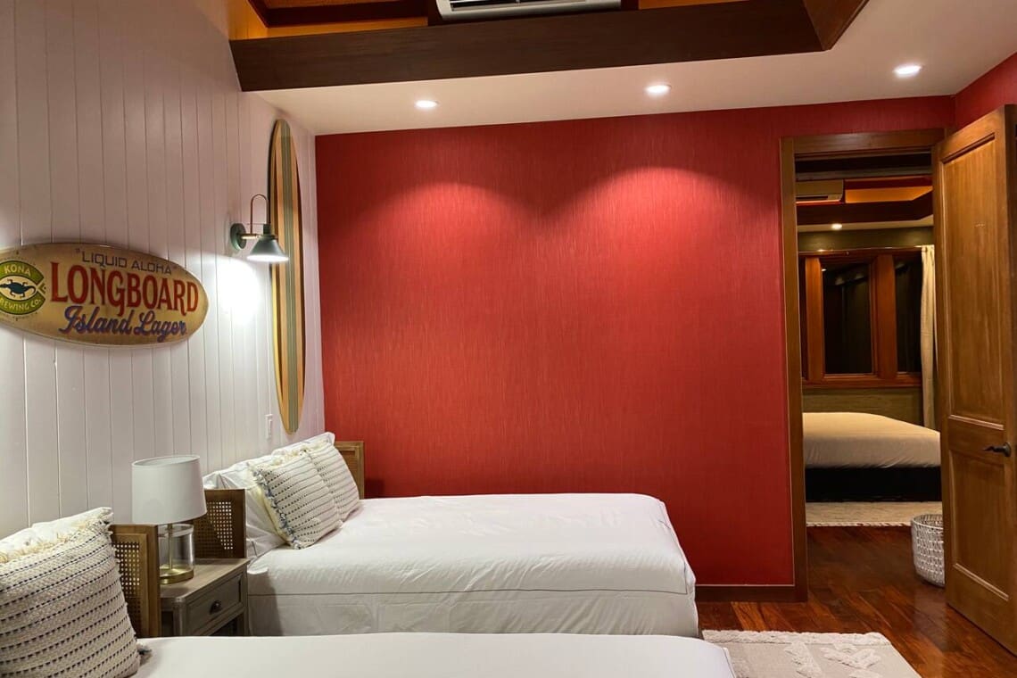A bedroom with two beds, a red accent wall, and an open doorway providing a view into an adjacent bedroom.