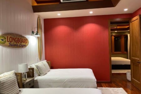 A bedroom with two beds, a red accent wall, and an open doorway providing a view into an adjacent bedroom.