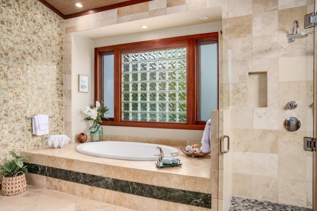 Spacious primary bathroom at Hale Mele with a soaking tub, walk-in rain shower, and elegant stone finishes in Mauna Lani, Hawaiʻi.