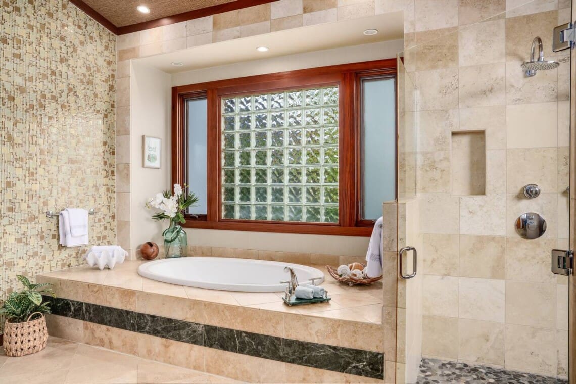 Spacious primary bathroom at Hale Mele with a soaking tub, walk-in rain shower, and elegant stone finishes in Mauna Lani, Hawaiʻi.