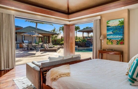 A bright bedroom with large corner pocket doors fully opened to a sunny backyard patio featuring a pool, sun loungers, and an outdoor dining area.