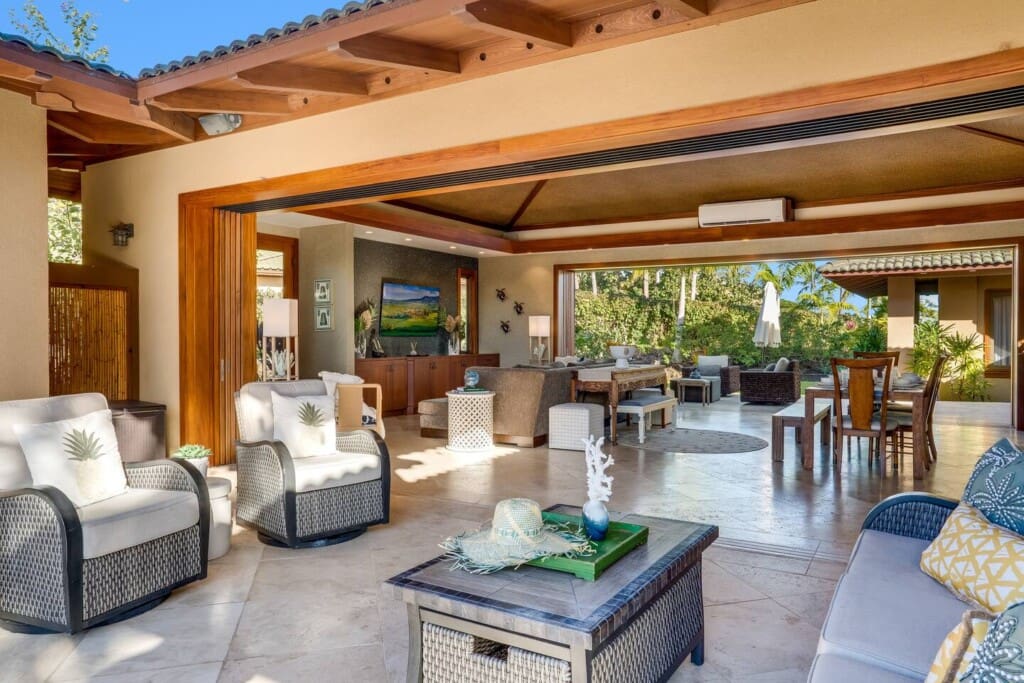 An open-concept living room with large wood pocket doors fully opened to an outdoor patio with wicker lounge seating.