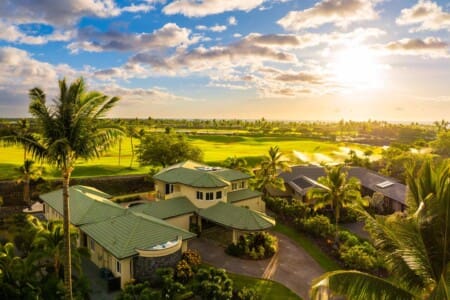 Aerial view of Hale Mele overlooking palm trees, a golf course, and the Kohala Coast at sunset.