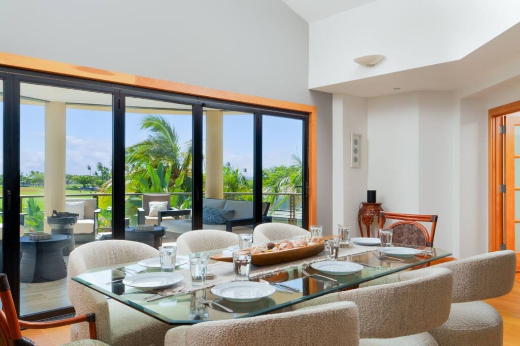 An indoor dining table set with plates and glasses next to large windows overlooking an outdoor lanai.