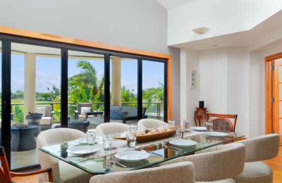 An indoor dining table set with plates and glasses next to large windows overlooking an outdoor lanai.