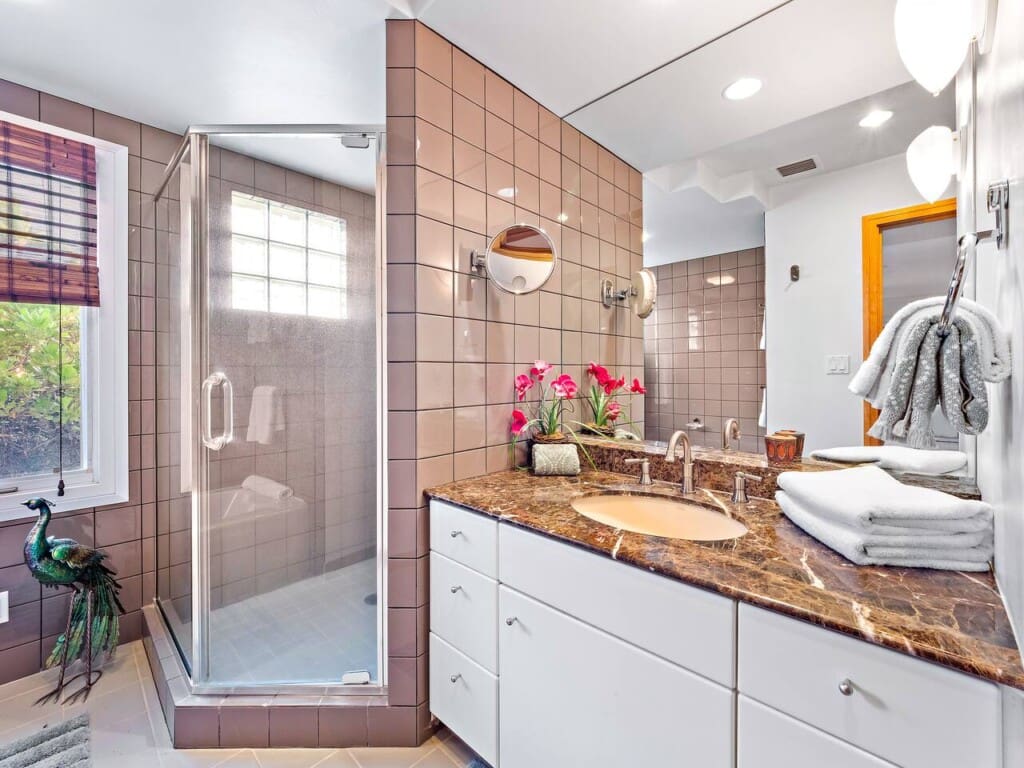 An en-suite bathroom featuring a granite vanity countertop, pinkish-brown wall tiles, and a glass-enclosed walk-in shower.
