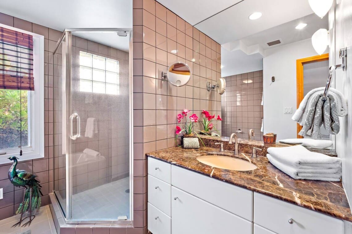 An en-suite bathroom featuring a granite vanity countertop, pinkish-brown wall tiles, and a glass-enclosed walk-in shower.