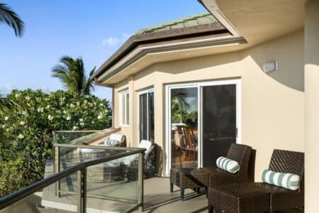 An upper-level private lanai at a luxury vacation rental in Mauna Lani, featuring wicker lounge chairs and tropical greenery.