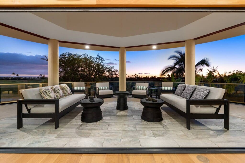 Covered outdoor lanai with cushioned seating overlooking palm trees and a golf course at Hale Mele.