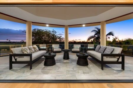 Covered outdoor lanai with cushioned seating overlooking palm trees and a golf course at Hale Mele.