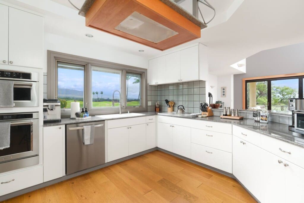 A bright gourmet kitchen with white cabinetry, granite countertops, stainless steel appliances, and a window overlooking a golf course.