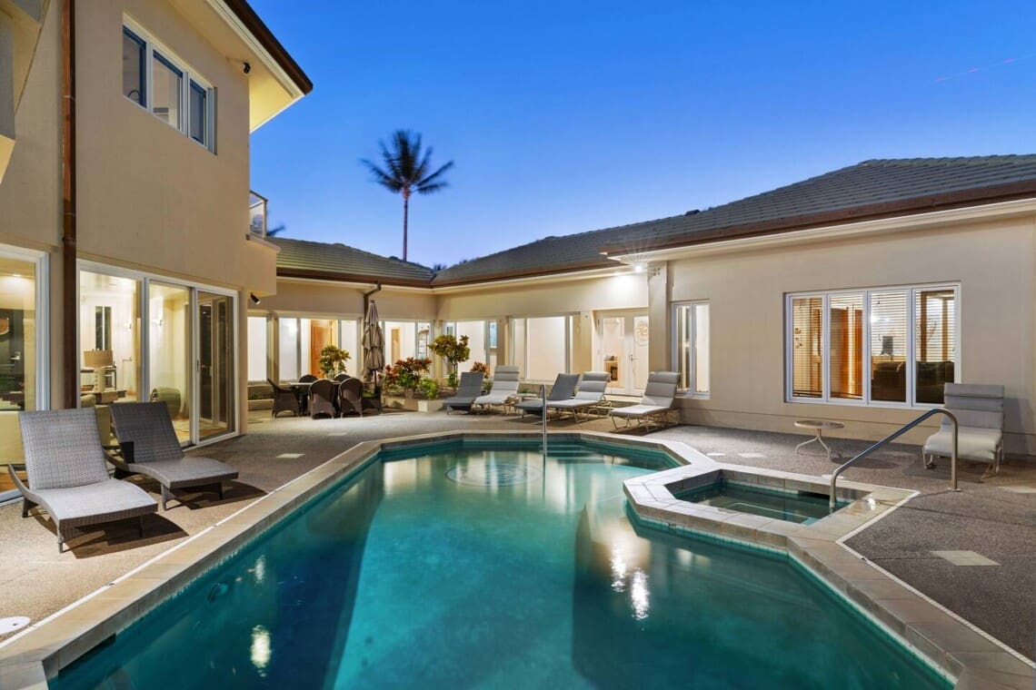 Private pool and spa surrounded by lounge chairs and illuminated outdoor living spaces at dusk.