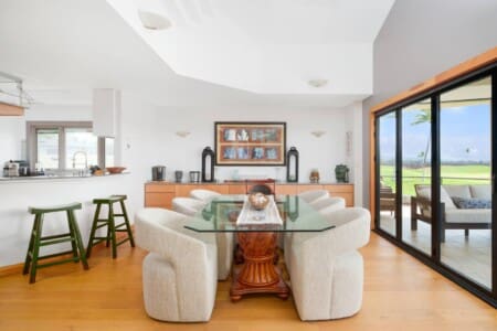 An open-concept dining room with a glass-top table, upholstered chairs, kitchen barstools, and sliding glass doors to the lanai.