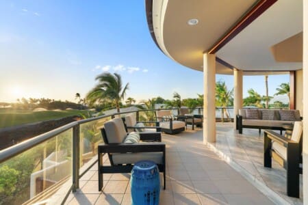 Covered lanai with lounge seating overlooking palm trees and the Mauna Lani golf course at sunset.