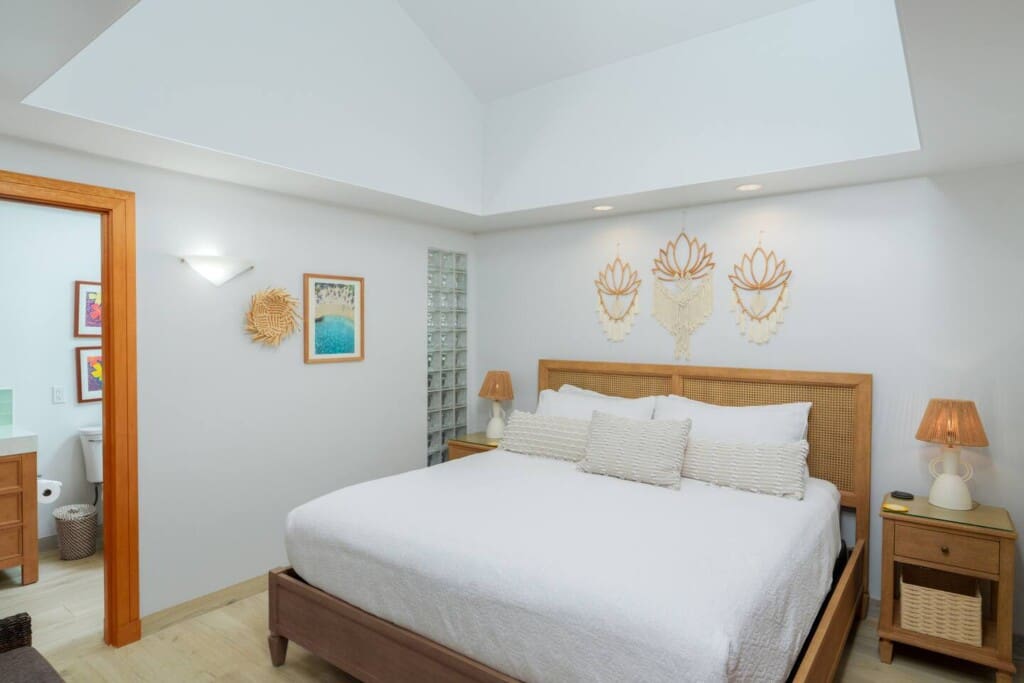 Bright primary bedroom at a Mauna Lani vacation home with a large bed, woven headboard, and en-suite bathroom access.