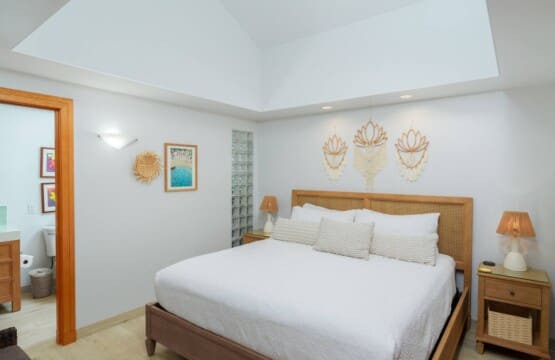 Bright primary bedroom at a Mauna Lani vacation home with a large bed, woven headboard, and en-suite bathroom access.
