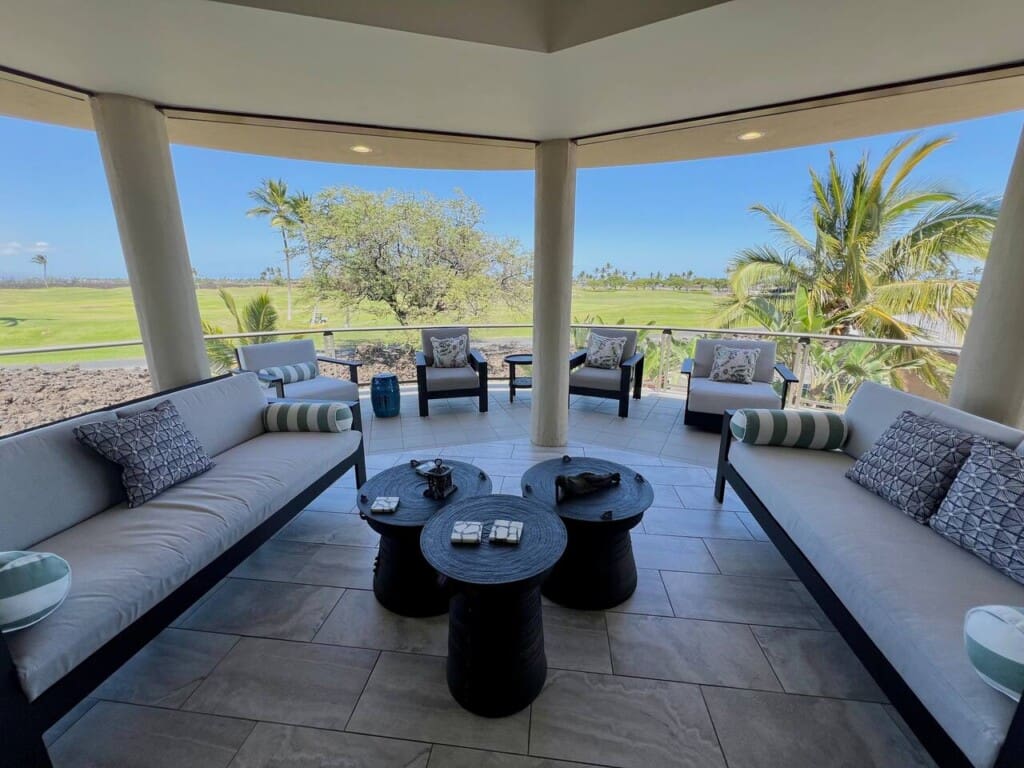 Covered lanai with cushioned lounge seating overlooking palm trees and the Mauna Lani golf course.