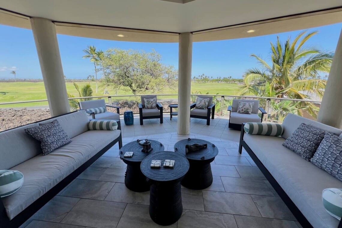 Covered lanai with cushioned lounge seating overlooking palm trees and the Mauna Lani golf course.