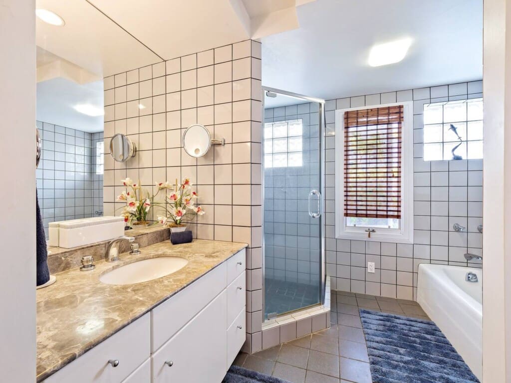 Bright bathroom featuring a marble vanity, tiled walls, a glass-enclosed walk-in shower, and a separate bathtub.