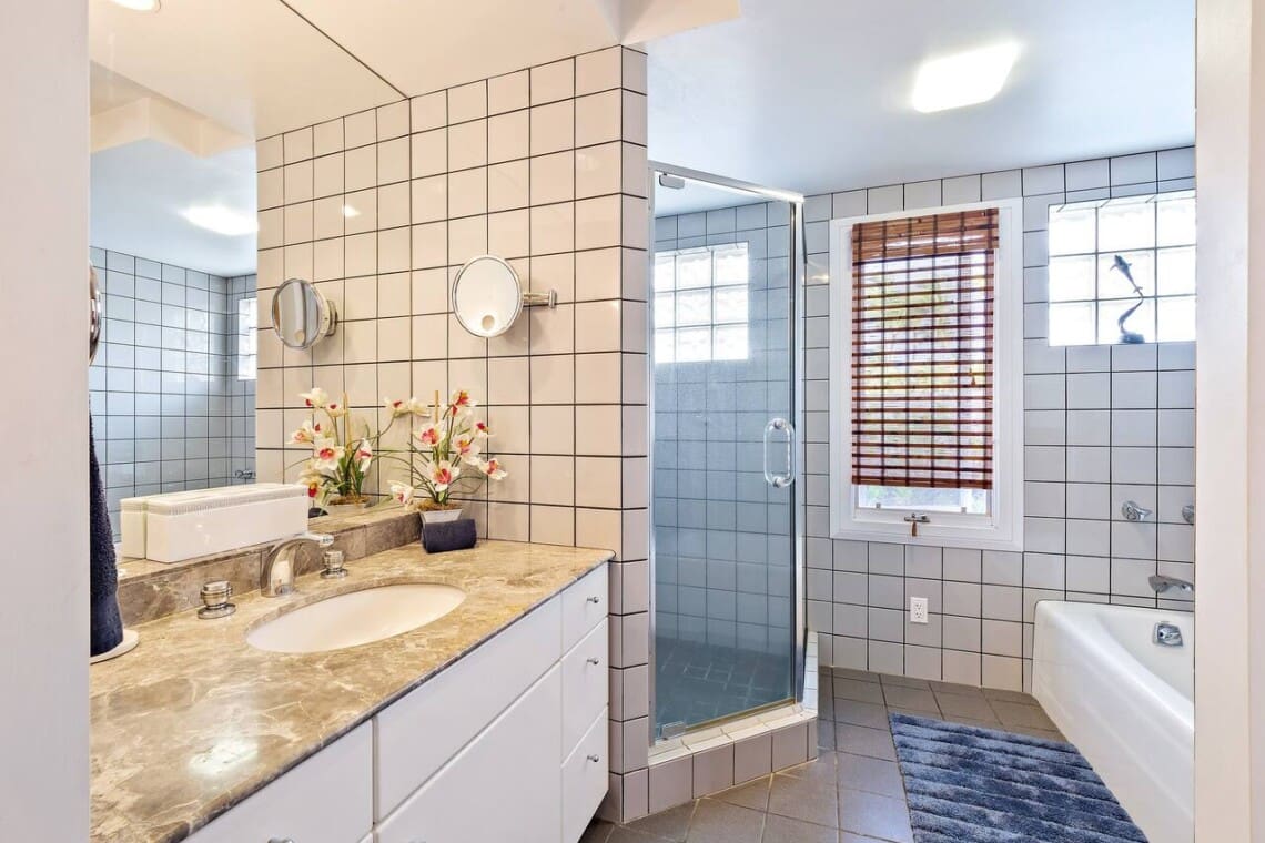 Bright bathroom featuring a marble vanity, tiled walls, a glass-enclosed walk-in shower, and a separate bathtub.