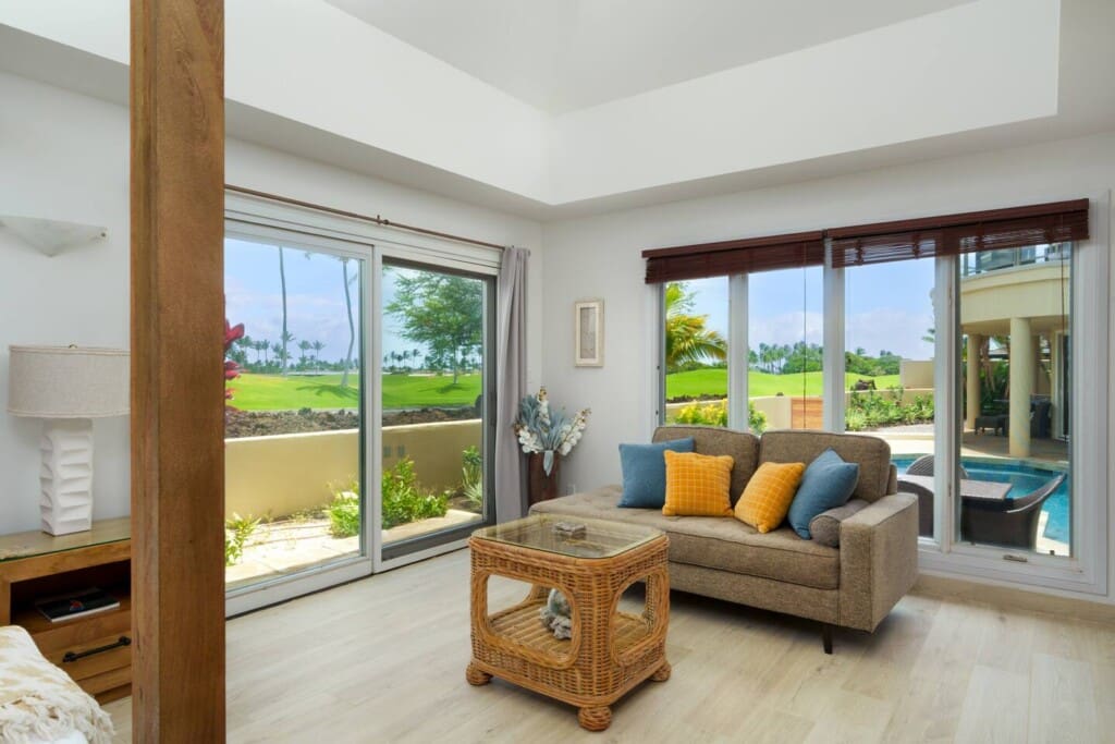 Bright guest suite at Hale Mele with a four-poster king bed, seating area, and private lanai overlooking tropical landscaping in Mauna Lani.