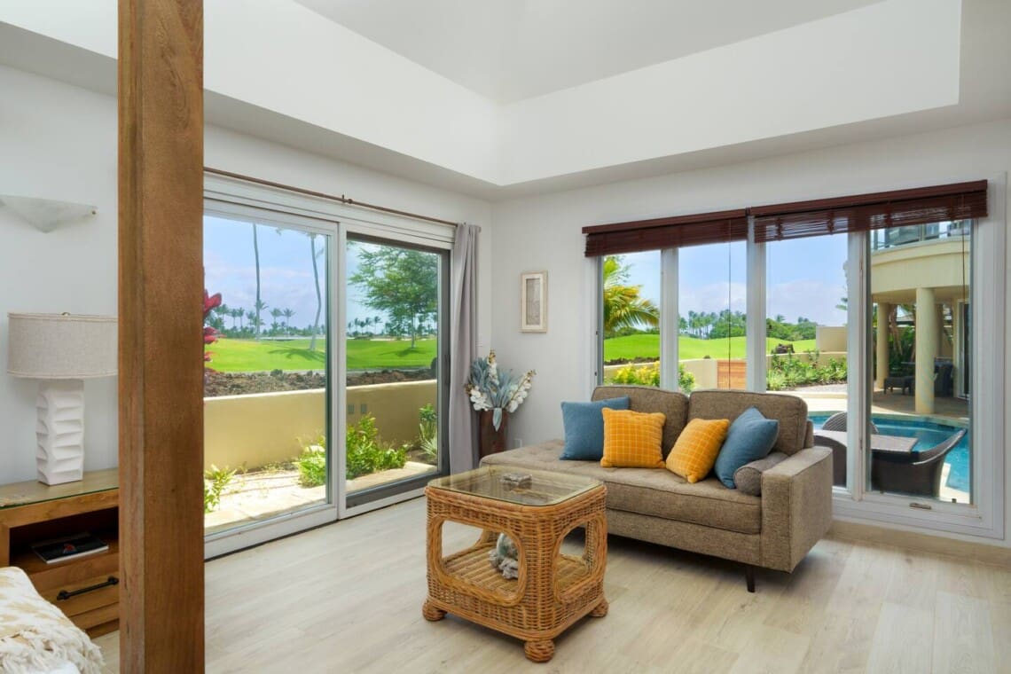 Bright guest suite at Hale Mele with a four-poster king bed, seating area, and private lanai overlooking tropical landscaping in Mauna Lani.