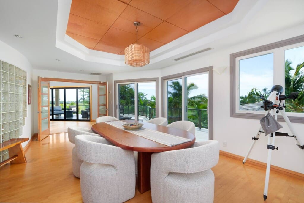 A bright secondary dining or meeting room with an oval wooden table, upholstered chairs, and a telescope near a window.