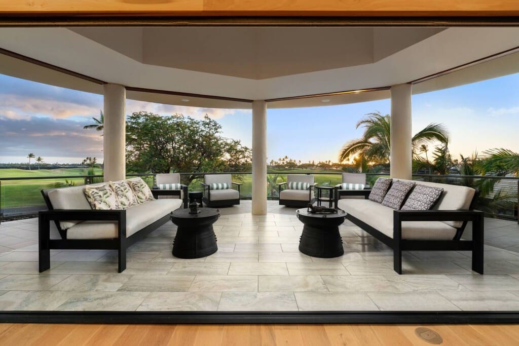Covered outdoor lanai with lounge seating overlooking the Mauna Lani golf course at sunset.