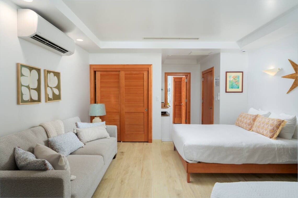 Bright guest bedroom suite featuring a comfortable sofa seating area, a large bed, and wooden closet doors.
