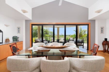An indoor dining area with a glass-top table looking out through large glass doors to an outdoor lanai.