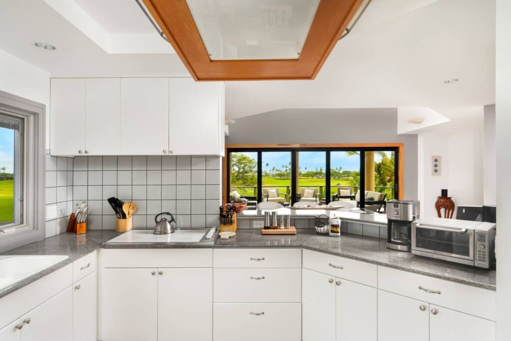 A kitchen with white cabinets, granite countertops, and a passthrough overlooking an open-concept dining room and outdoor lanai.