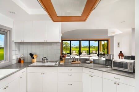 A kitchen with white cabinets, granite countertops, and a passthrough overlooking an open-concept dining room and outdoor lanai.