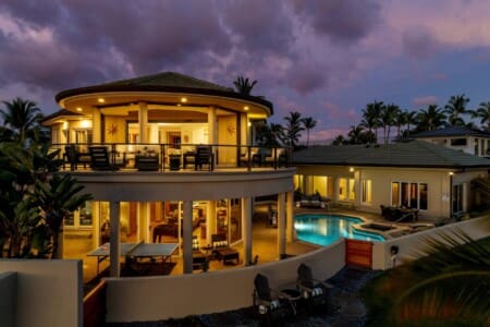 Twilight exterior view of Hale Mele with illuminated lanai, private pool, spa, and tropical landscaping.